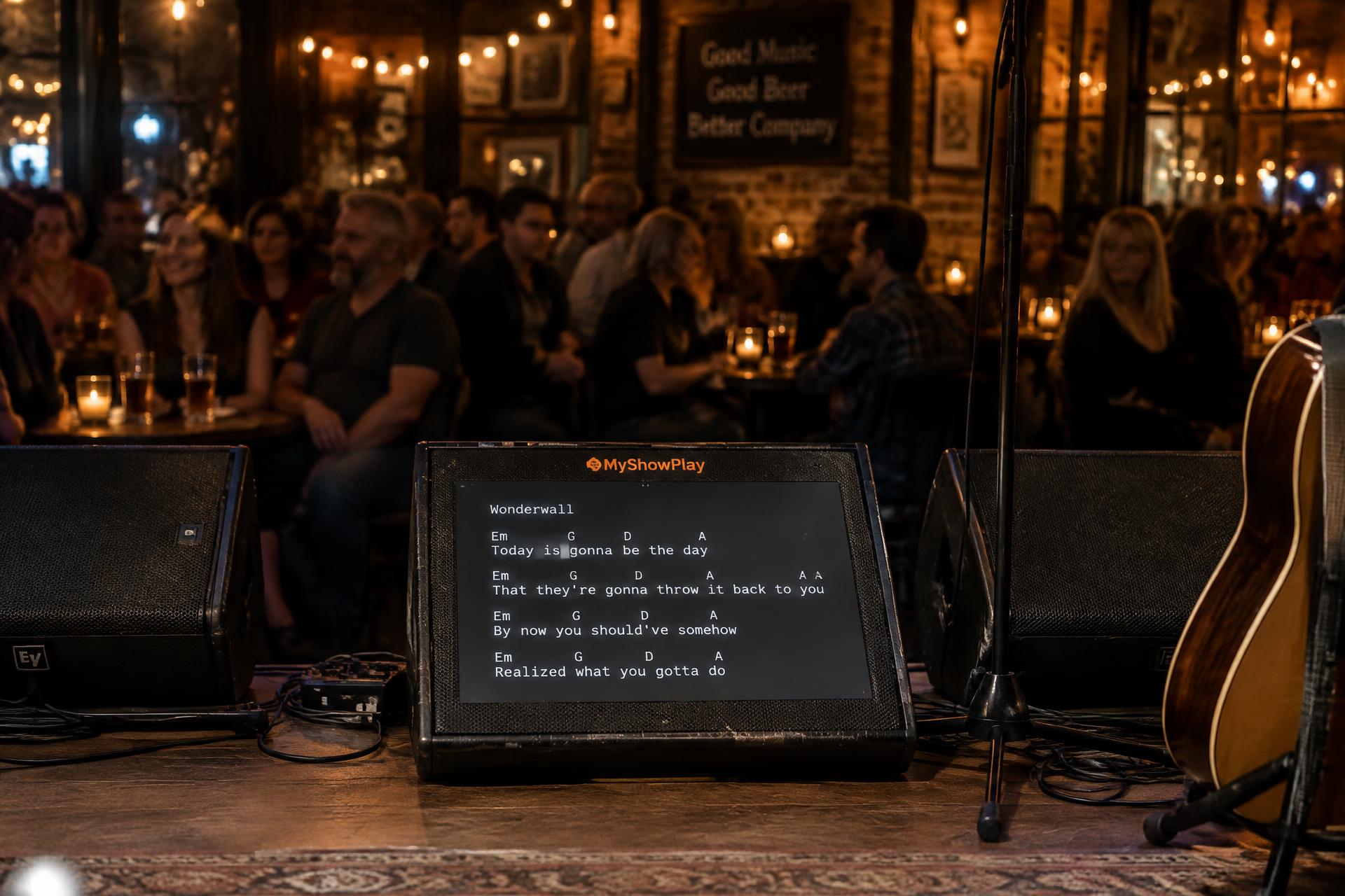 Palco de pub visto do fundo: monitor de chão entre caixas de retorno exibindo a cifra do MyShowPlay para a plateia